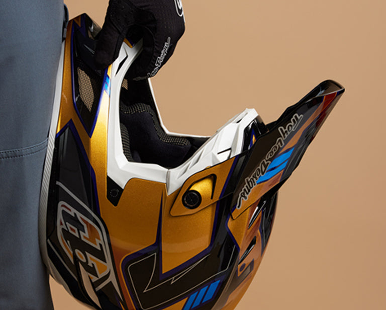 Un cavalier tenant un casque intégral Troy Lee Designs devant un fond marron